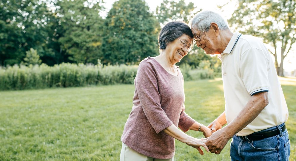 Photo of a couple in their 60s or 70s holding hands while pressing their foreheads against one another and smiling.